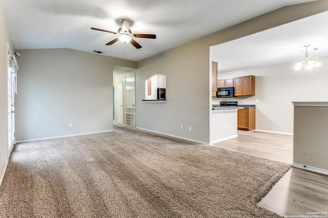 unfurnished living room with visible vents, light wood-style floors, baseboards, ceiling fan with notable chandelier, and vaulted ceiling
