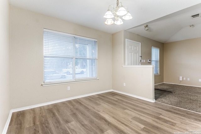 empty room with baseboards, visible vents, wood finished floors, and a notable chandelier