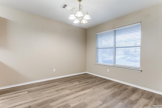 spare room with light wood-type flooring, baseboards, a notable chandelier, and visible vents