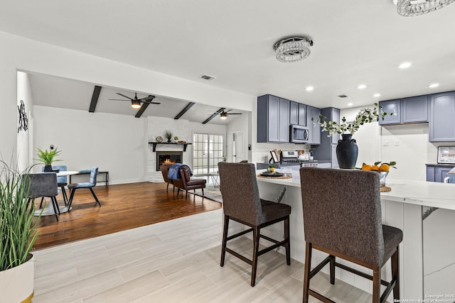 dining space featuring ceiling fan, lofted ceiling with beams, a fireplace, light wood-type flooring, and visible vents
