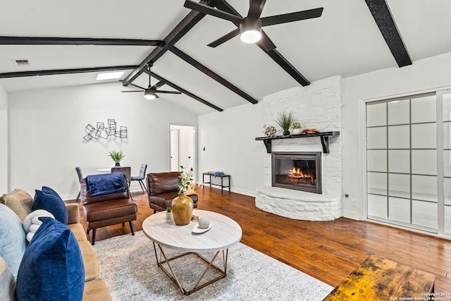 living area with wood-type flooring, visible vents, a stone fireplace, ceiling fan, and vaulted ceiling with beams
