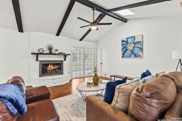 living area with ceiling fan, a stone fireplace, wood finished floors, and lofted ceiling with skylight