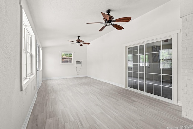 interior space with light wood-style flooring, a ceiling fan, baseboards, lofted ceiling, and a wall mounted AC