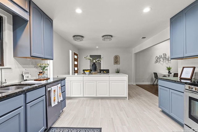 kitchen featuring a sink, appliances with stainless steel finishes, blue cabinets, and dark stone countertops