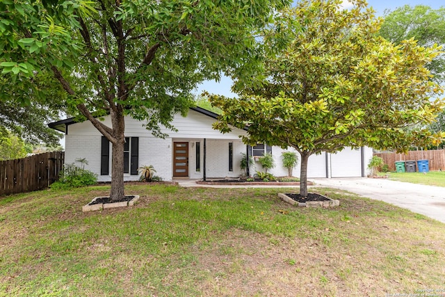 view of property hidden behind natural elements featuring concrete driveway, brick siding, fence, and a front yard