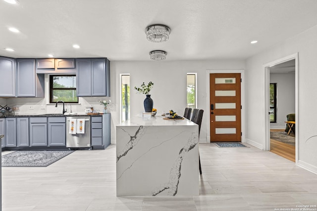 kitchen with stainless steel dishwasher, a sink, recessed lighting, and light stone countertops