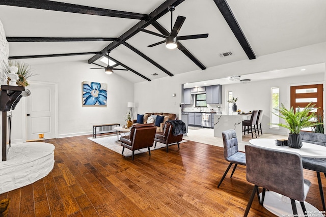 living area featuring visible vents, wood finished floors, baseboards, ceiling fan, and vaulted ceiling with beams