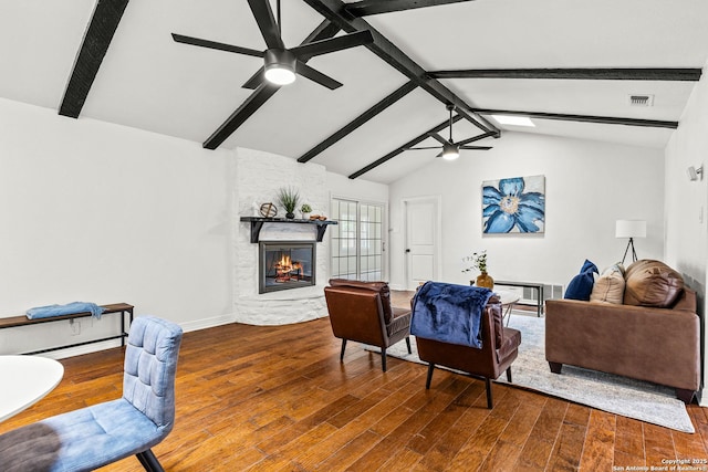 living room with visible vents, wood finished floors, a stone fireplace, lofted ceiling with beams, and a ceiling fan