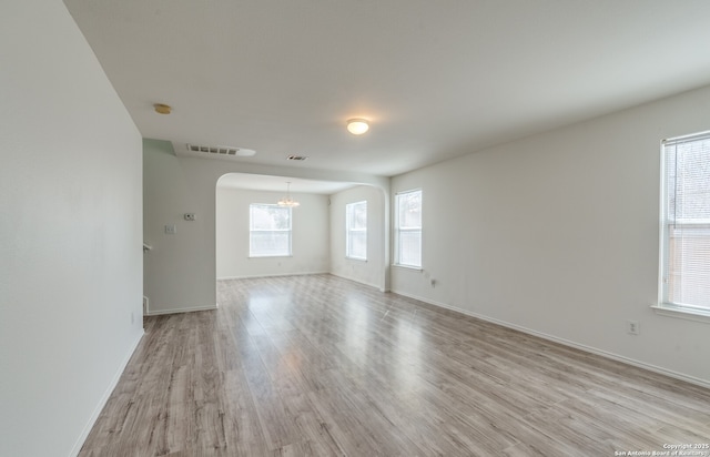 unfurnished room featuring visible vents, baseboards, arched walkways, light wood-style flooring, and a notable chandelier