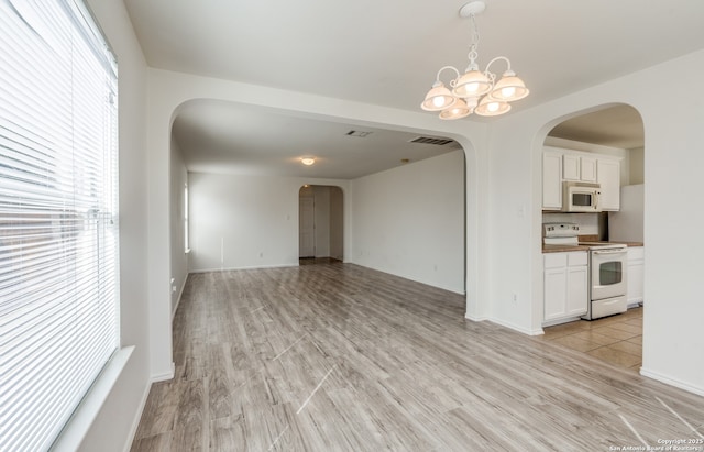 unfurnished living room featuring visible vents, arched walkways, light wood-style flooring, and an inviting chandelier