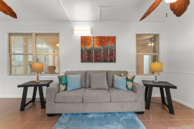 tiled living area with a ceiling fan and a wainscoted wall