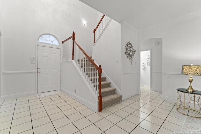 foyer featuring arched walkways, baseboards, light tile patterned floors, and stairway