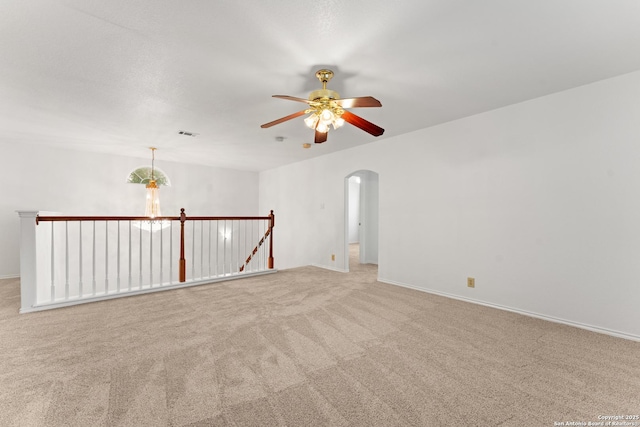 carpeted empty room featuring baseboards, a ceiling fan, arched walkways, and visible vents