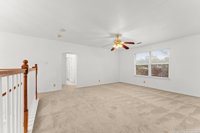 unfurnished room with visible vents, baseboards, light colored carpet, arched walkways, and a ceiling fan