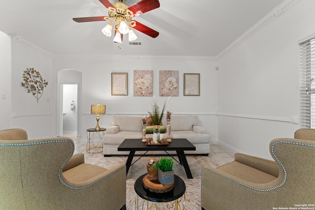 tiled living room with arched walkways, a ceiling fan, baseboards, visible vents, and ornamental molding