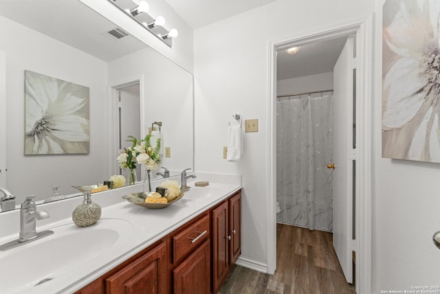 full bath with double vanity, visible vents, a sink, and wood finished floors