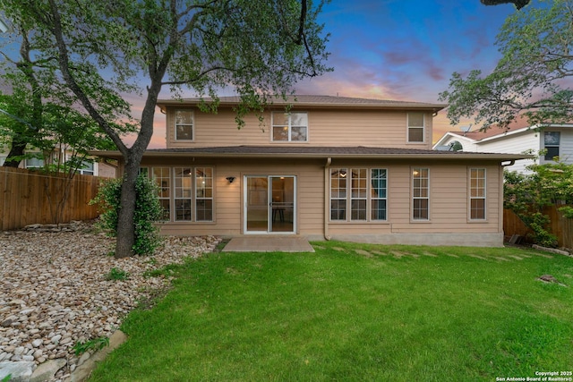 back of property at dusk featuring a fenced backyard and a yard