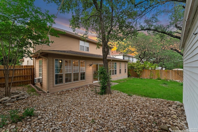 back of house at dusk with a yard and a fenced backyard