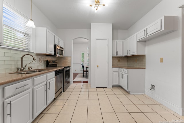 kitchen featuring arched walkways, white cabinets, a sink, appliances with stainless steel finishes, and backsplash