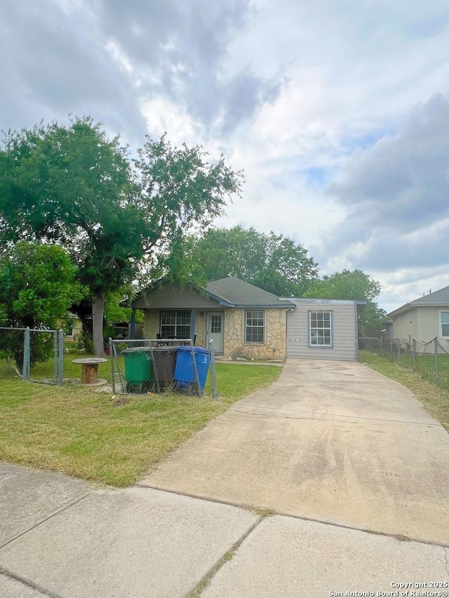 view of front of home with fence, concrete driveway, a front lawn, and stone siding