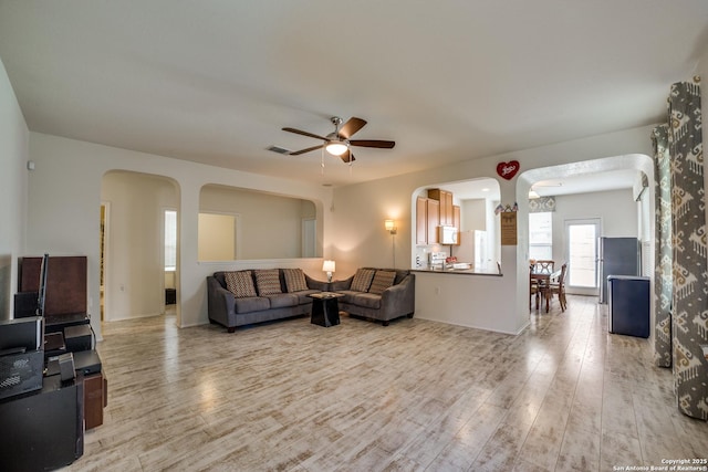 living room with arched walkways, a ceiling fan, and light wood-type flooring