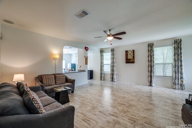 living room with a ceiling fan, arched walkways, visible vents, and wood finished floors
