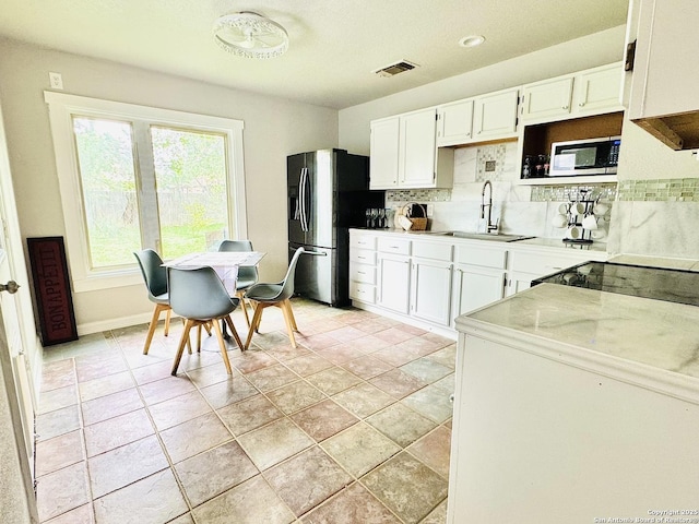kitchen with backsplash, visible vents, a sink, white cabinets, and stainless steel fridge