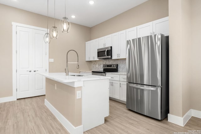 kitchen featuring a kitchen island with sink, white cabinets, tasteful backsplash, a sink, and stainless steel appliances
