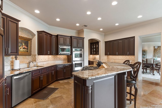 kitchen featuring light stone countertops, a breakfast bar, arched walkways, a sink, and stainless steel appliances
