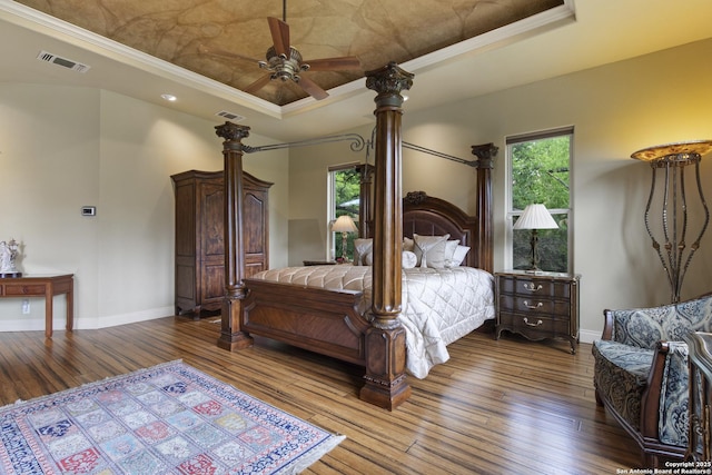 bedroom with a tray ceiling, visible vents, baseboards, and hardwood / wood-style floors
