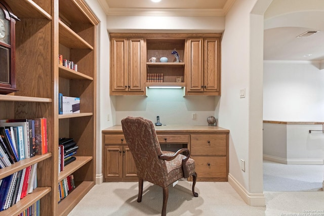 home office with ornamental molding, built in desk, and light colored carpet