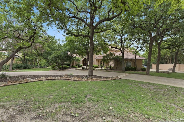 view of front facade featuring a tiled roof, fence, curved driveway, and a front yard