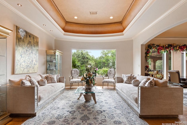 living room with crown molding, arched walkways, wood finished floors, and a raised ceiling