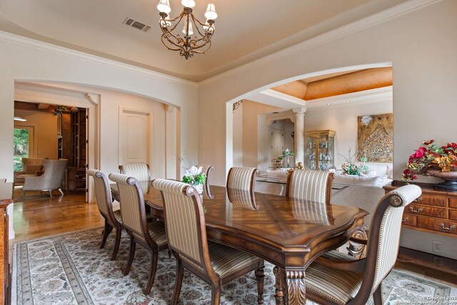 dining room featuring visible vents, crown molding, arched walkways, wood finished floors, and an inviting chandelier