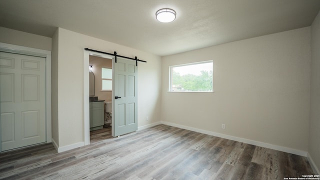 5806 Gillis, San Antonio, TX 78240 - unfurnished bedroom featuring baseboards, ensuite bath, a barn door, and light wood-type flooring