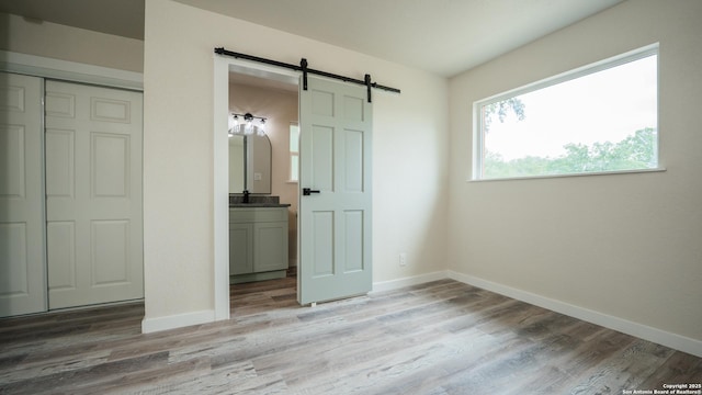 5806 Gillis, San Antonio, TX 78240 - unfurnished bedroom with baseboards, a barn door, and light wood-type flooring