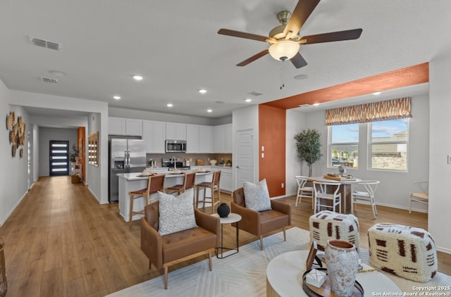living room with baseboards, ceiling fan, light wood-type flooring, and visible vents