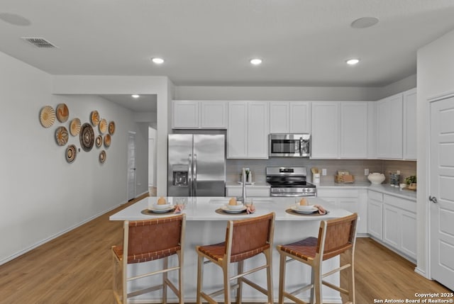 kitchen with visible vents, a kitchen breakfast bar, light wood-type flooring, tasteful backsplash, and stainless steel appliances