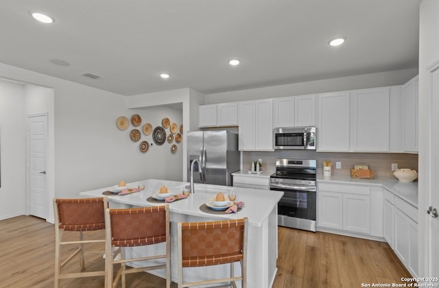 kitchen featuring light countertops, appliances with stainless steel finishes, a kitchen island with sink, and tasteful backsplash