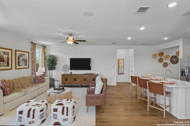 living area featuring light wood finished floors, a ceiling fan, baseboards, recessed lighting, and visible vents