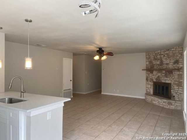kitchen with a ceiling fan, a fireplace, open floor plan, light countertops, and a sink