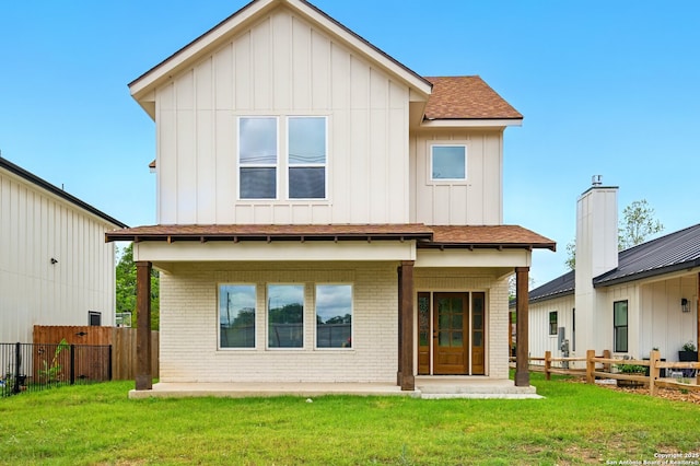 rear view of property with fence, board and batten siding, a yard, and brick siding