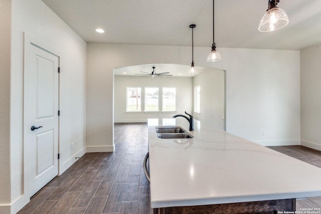 kitchen with a sink, baseboards, a ceiling fan, and dark wood-style flooring