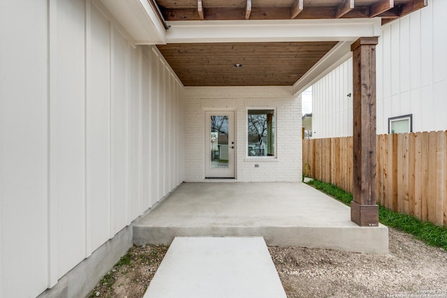doorway to property with fence, a patio, board and batten siding, and brick siding