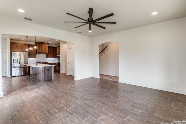 unfurnished living room with arched walkways, a ceiling fan, visible vents, and baseboards