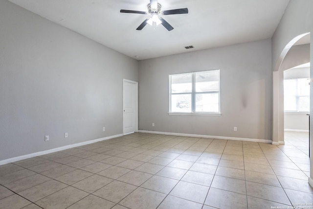 empty room with ceiling fan, visible vents, arched walkways, baseboards, and light tile patterned flooring