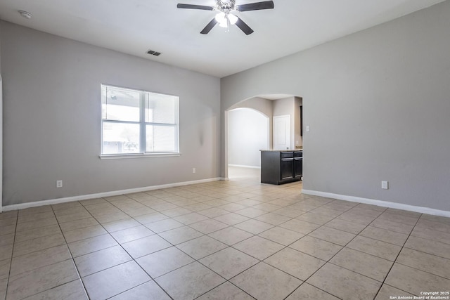 spare room with ceiling fan, visible vents, arched walkways, light tile patterned floors, and baseboards