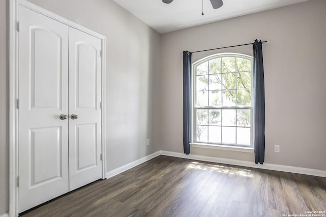 unfurnished room with baseboards, a ceiling fan, and dark wood-style flooring