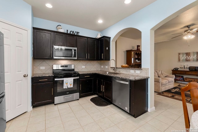 kitchen featuring decorative backsplash, appliances with stainless steel finishes, a sink, open floor plan, and stone counters