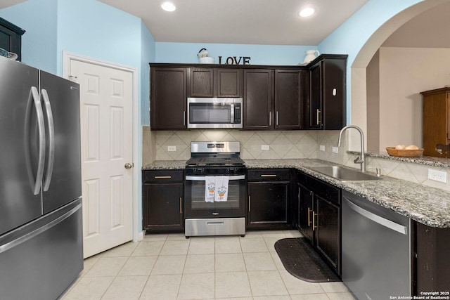 kitchen featuring appliances with stainless steel finishes, arched walkways, light stone countertops, a sink, and light tile patterned floors
